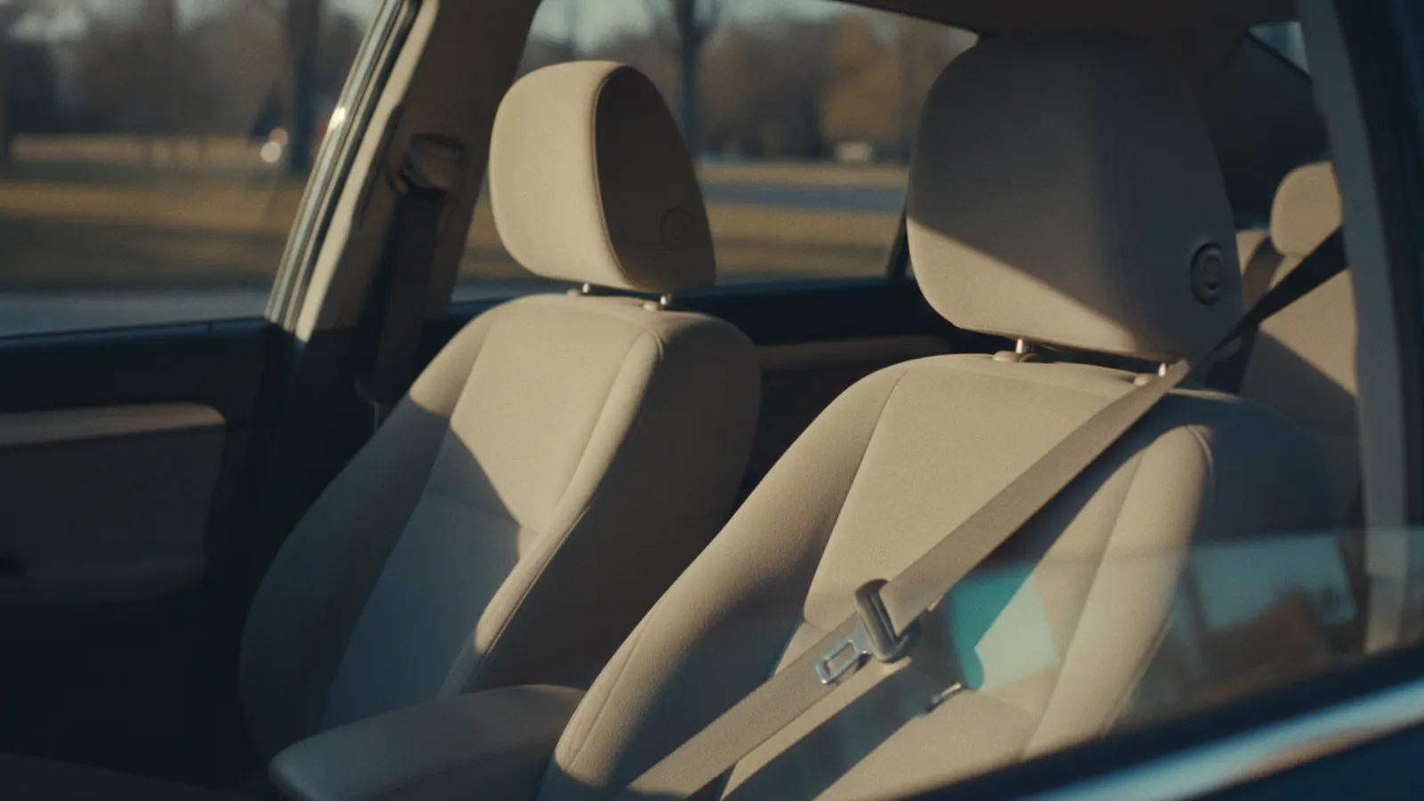 The empty front passenger seat of a stationary parked car in warm daylight, its belt fastened across nothing.